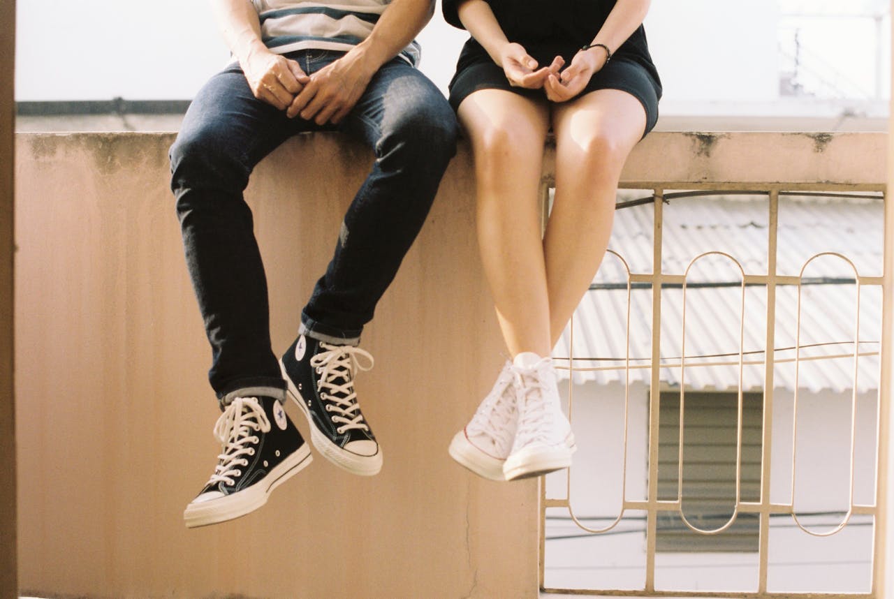 Services-03 A relaxed couple sitting on a ledge, wearing stylish sneakers, showcasing togetherness.