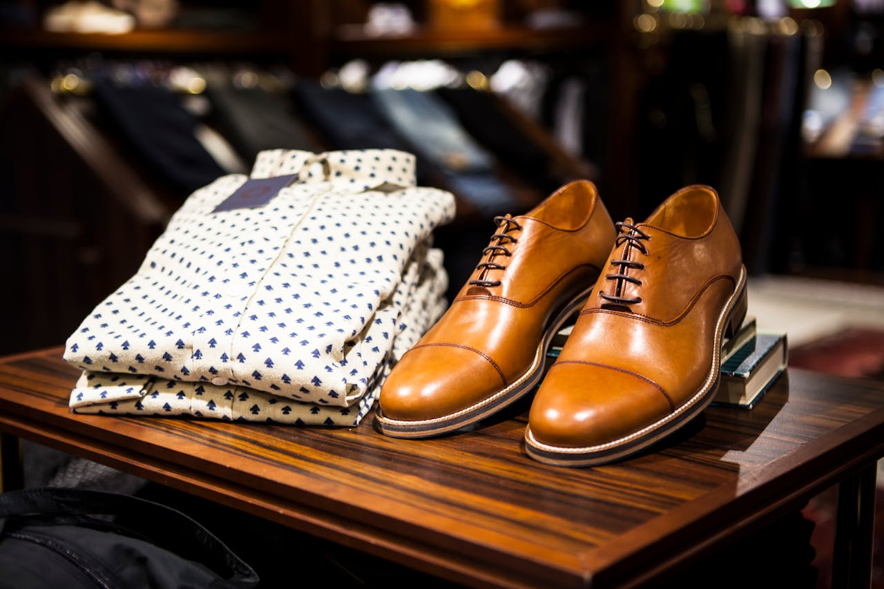 Services-01 Elegant brown leather shoes and printed shirt displayed on a wooden table in a stylish clothing store.